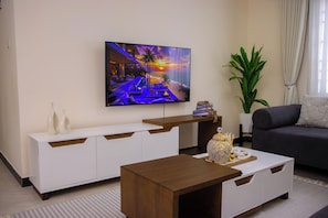 Un salon moderne avec un téléviseur à écran plat, une table basse en bois, un canapé gris et un meuble console blanc.