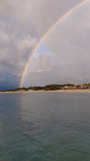 A beach with a rainbow over the water, buildings in the background, and a cloudy sky. - Villa in the center of Bastelicaccia with a pool, in a quiet location, and a large garden (Bastelicaccia)