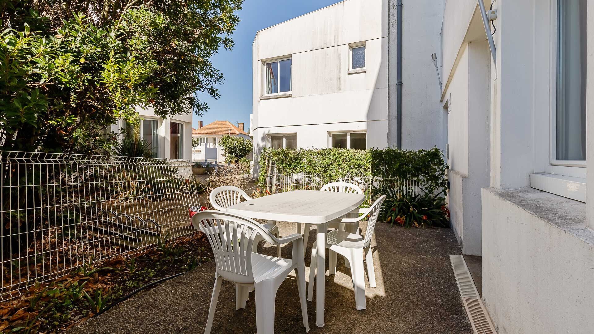 A patio with a table and chairs, surrounded by a fence and greenery.