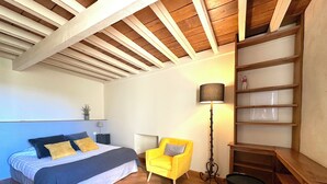 A bedroom with a bed, a yellow armchair, a floor lamp, and a wooden shelf unit. - Billebaude guest room -Breakfast included (Montoillot)
