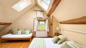 A bedroom with a sloped ceiling, wooden beams, a bed with green pillows, a window with curtains, and a radiator. - Biche Blanche guest room - Breakfast included (Montoillot)