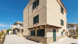 A two-story building with a stone facade, green shutters, and a tiled entrance. - AffittaSardegna - Quadri Tramonto  (Lu Bagnu)