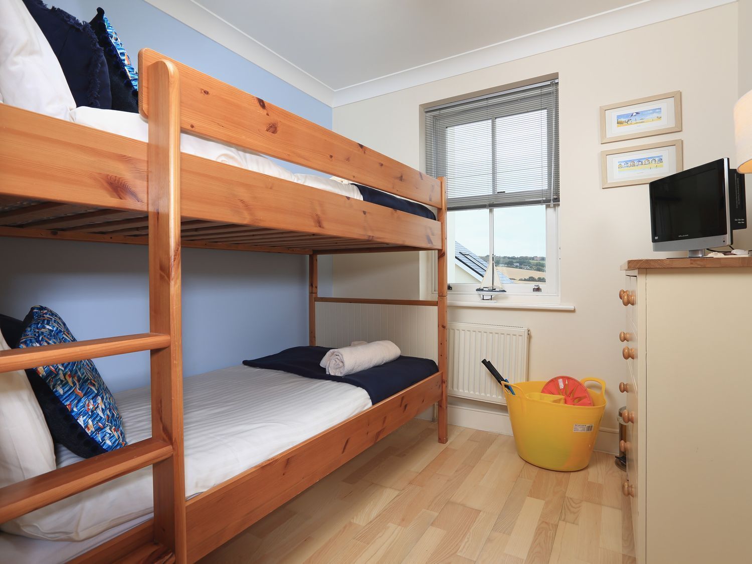 Quarto com beliche, uma janela, uma escrivaninha com computador e um balde amarelo.