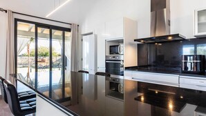 A modern kitchen with a black countertop, stainless steel appliances, and a glass door leading to an outdoor area. - 2 Cortons - Wall (Muro)