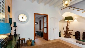 A room with a wooden floor, a green cabinet, a blue lamp, a round wall light, a wooden door, and a wall-mounted lamp. - Can Miguel (Sineu)