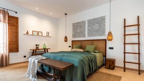 A bedroom with a bed, bedside tables, a bench, a ladder, and wall art. - Can Miguel (Sineu)