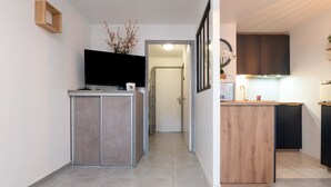 A modern kitchen with a flat-screen TV, wooden cabinets, and a small island with a sink. - Ty Avel Apartment with Shared Pool, Balcony, and Wi-Fi (Quiberon)