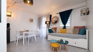 A compact living space with a dining area, a sofa with cushions, a small table with a mug, and a floor lamp. - Ty Avel Apartment with Shared Pool, Balcony, and Wi-Fi (Quiberon)