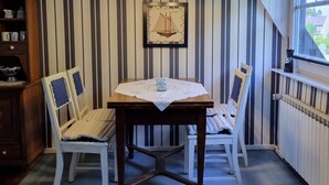 Een kamer met gestreept behang, een tafel met kantkleed, twee stoelen, een boekenkast en een lijst met afbeelding aan de muur.