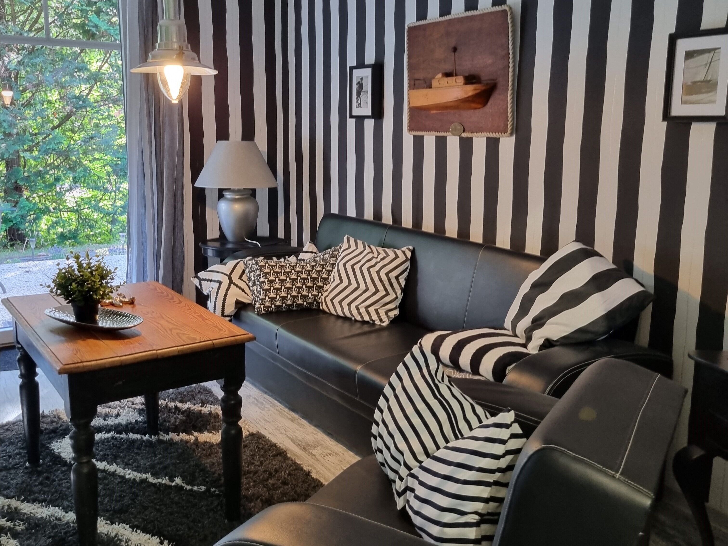 En moderne stue med væg i sort og hvide striber, en lædersofa og et træsofabord med en plante.
