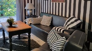 Ein modernes Wohnzimmer mit einer schwarz-weiß gestreiften Wand, einem Ledersofa und einem Couchtisch aus Holz mit einer Pflanze.