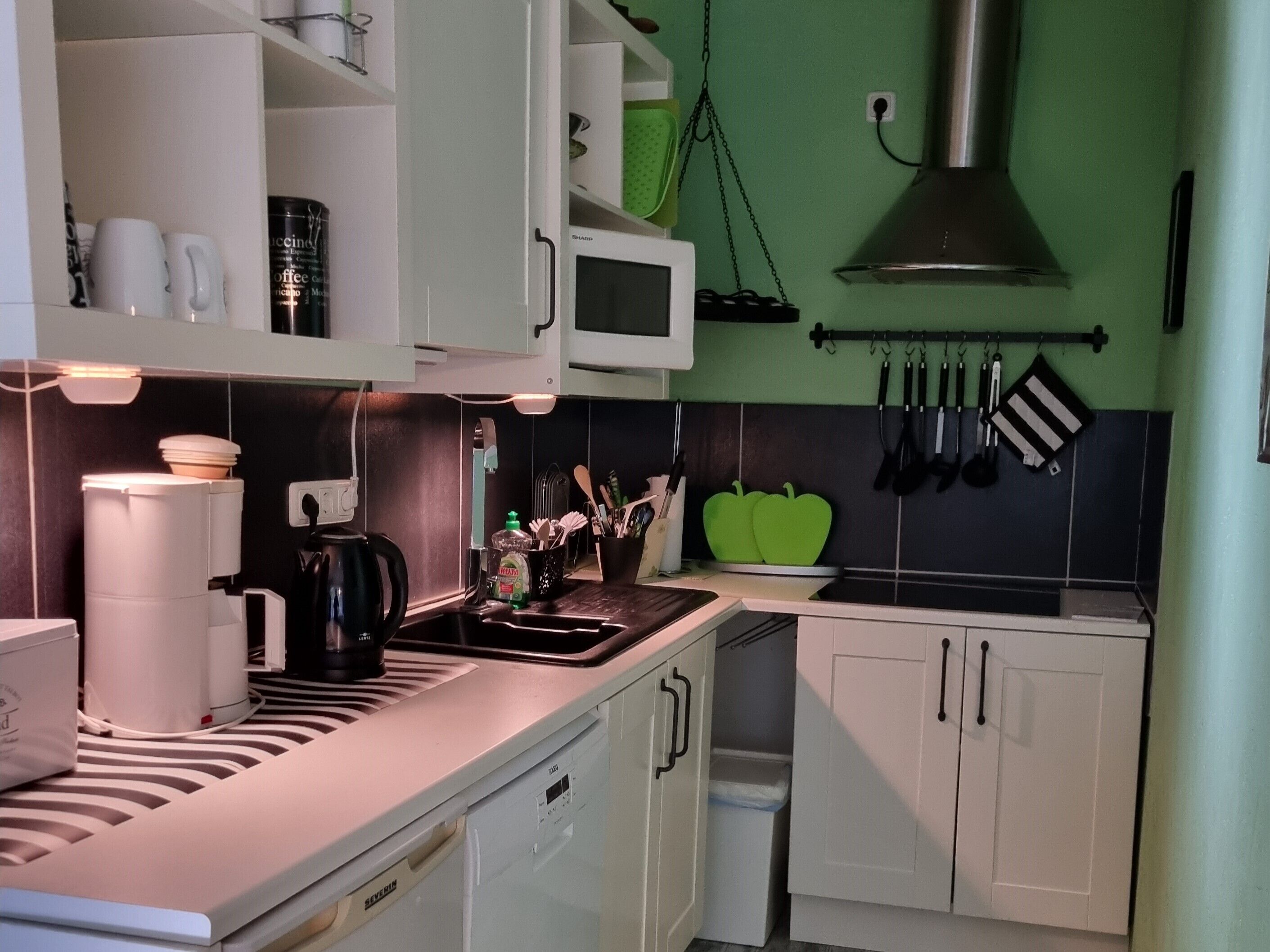A modern kitchen with white cabinets, a microwave, and a green wall.