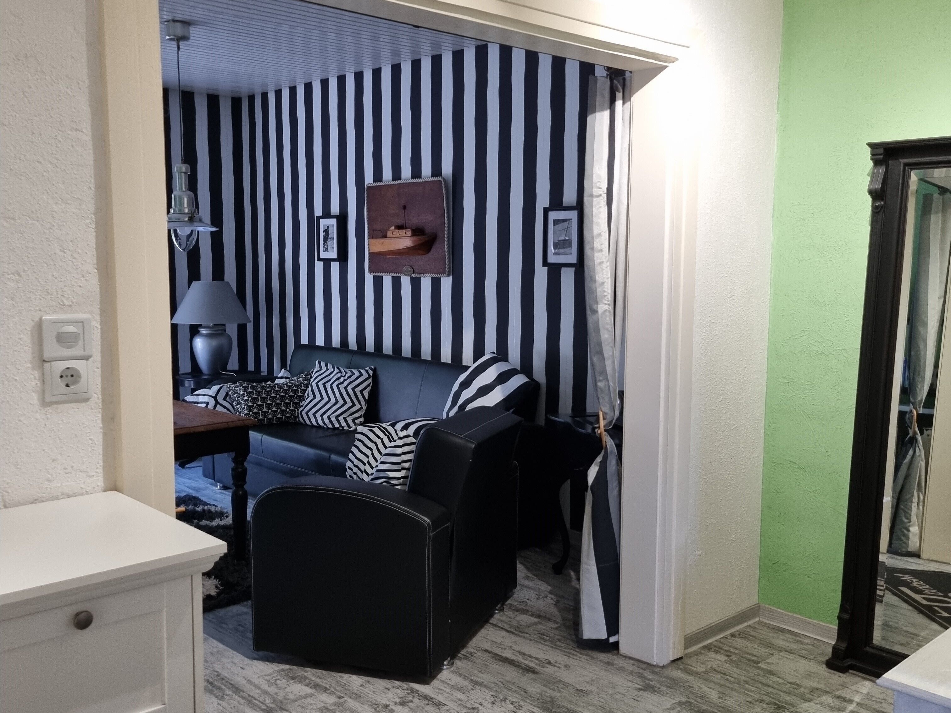 Quarto com parede listrada, sofá de couro preto, uma pequena mesa com abajur e parede verde.