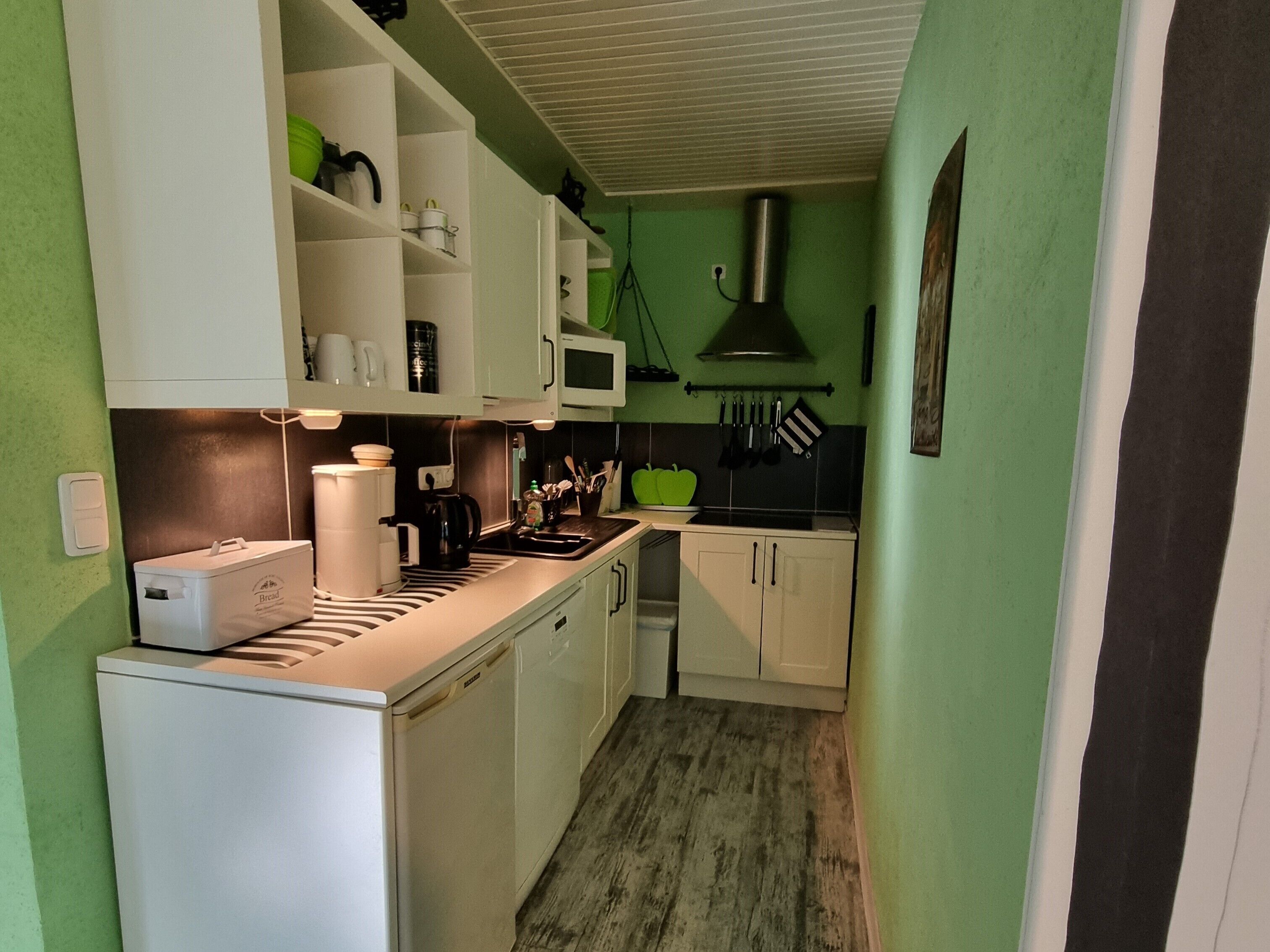 A compact kitchen with white cabinets, a microwave, a coffee maker, and a bread machine.