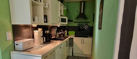A compact kitchen with white cabinets, a microwave, a coffee maker, and a bread machine.