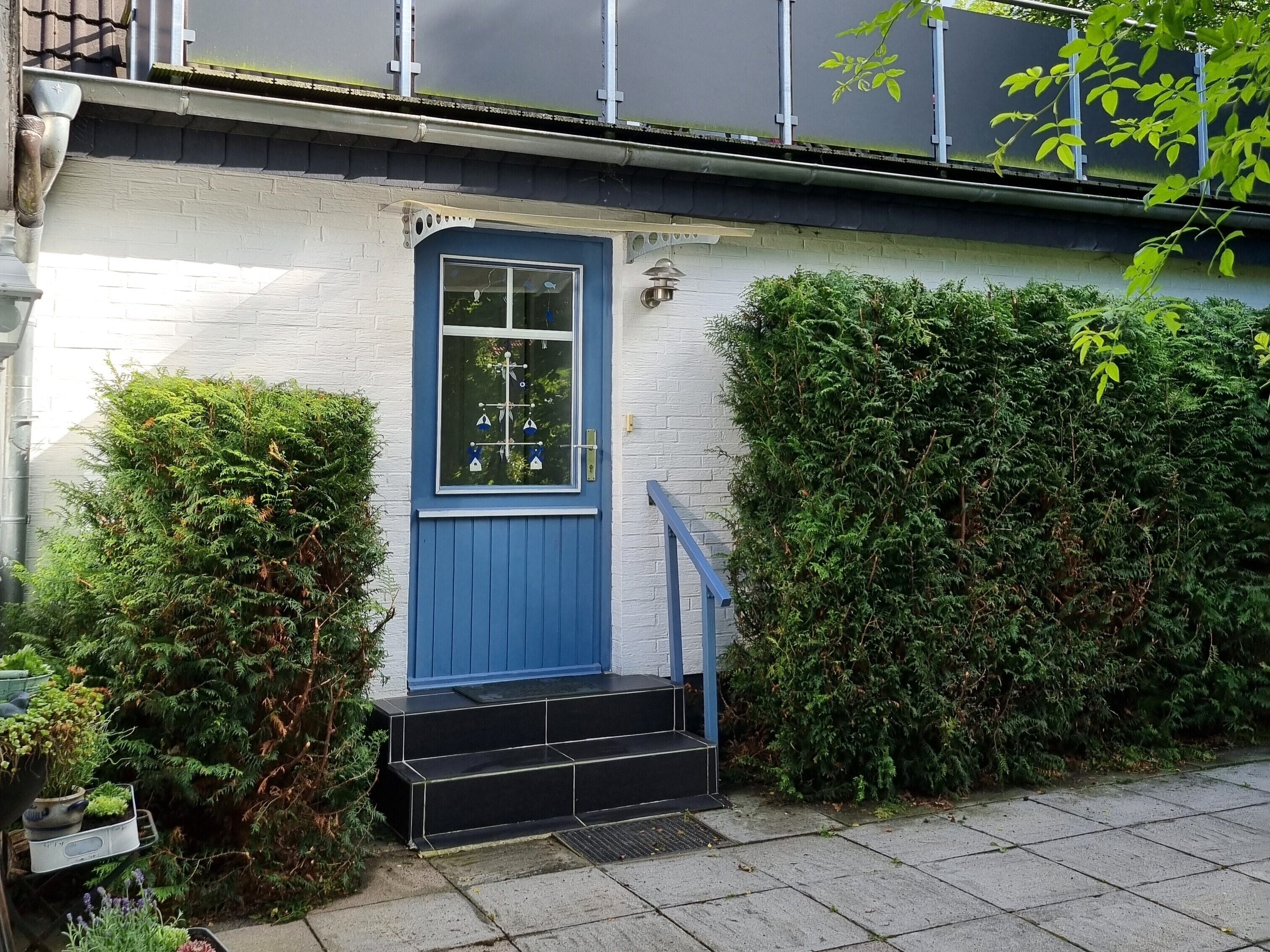 A house with a blue door, a small set of black steps leading to the entrance, and a white brick wall.