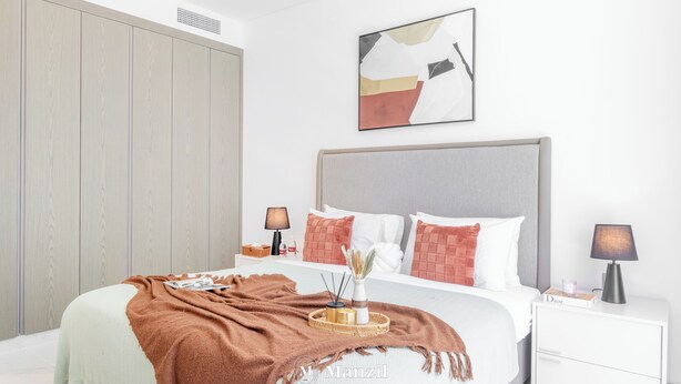 Ein modernes Schlafzimmer mit einem großen Bett, einem Kleiderschrank, einem Nachttisch mit Lampe und einem an der Wand hängenden abstrakten Gemälde.