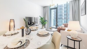 Ein modernes Wohnzimmer mit Essbereich, einer Couch, einem Fernseher und einem großen Fenster mit Vorhängen.