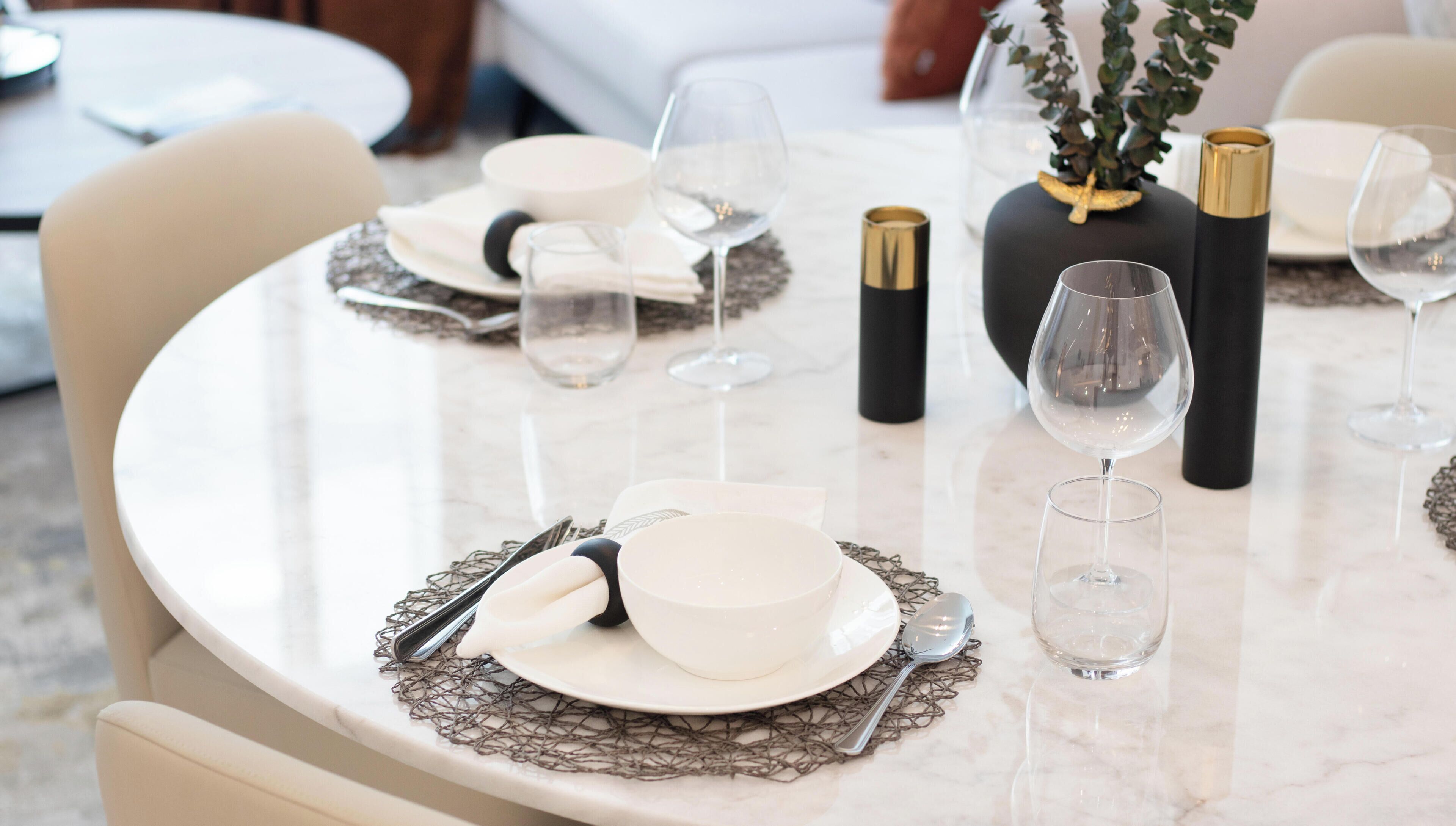 Eettafel gedekt met witte borden, kommen en bestek, met wijnglazen en zwarte vazen met gouden accenten.