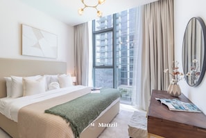 Um quarto moderno com uma cama grande, vista para a cidade pela janela, mesa de cabeceira com um vaso de flores e um espelho na parede.