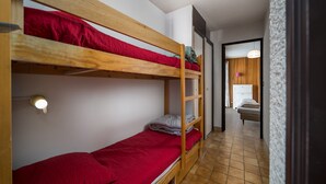 A dormitory room with bunk beds, a wooden door, and a hallway leading to another room. - Beautiful apartment with mountain views - sleeps 8 (Orcières)