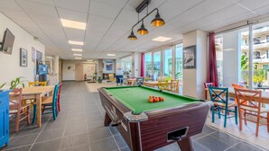A pool table in a well-lit room with large windows, chairs, and a casual seating area. - Bright apartment, balcony, sleeps 4 (Plougonvelin)
