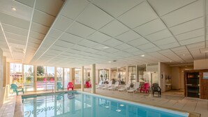 An indoor swimming pool with clear glass walls, surrounded by lounge chairs and a tiled floor. - Bright apartment, balcony, sleeps 4 (Plougonvelin)