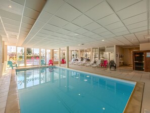 Ein überdachter Pool mit großen Glaswänden, umgeben von Liegestühlen und einem gefliesten Boden.