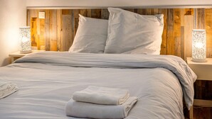 A neatly made bed with white linens and pillows, a wooden headboard, and two bedside lamps. - Bright apartment, balcony, sleeps 4 (Plougonvelin)