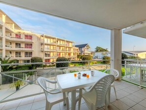 Ein Balkon mit Tisch und Stühlen, mit Blick auf ein Gebäude mit mehreren Balkonen und einem Garten.