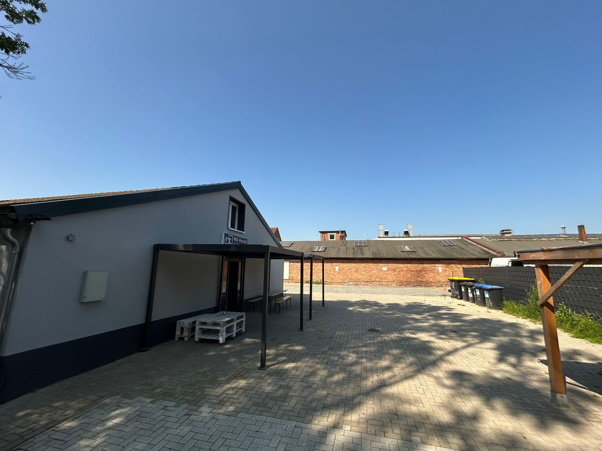 Un hostal con una zona de estar al aire libre techada, un edificio de ladrillo al fondo y un cielo despejado.