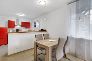 Une cuisine moderne avec des meubles de rangement rouges, une table à manger en bois et une vue à travers une fenêtre à carreaux.
