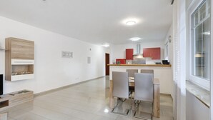 Eine moderne Küche mit weißen Schränken, ein Essbereich mit Stühlen und ein großes Fenster.