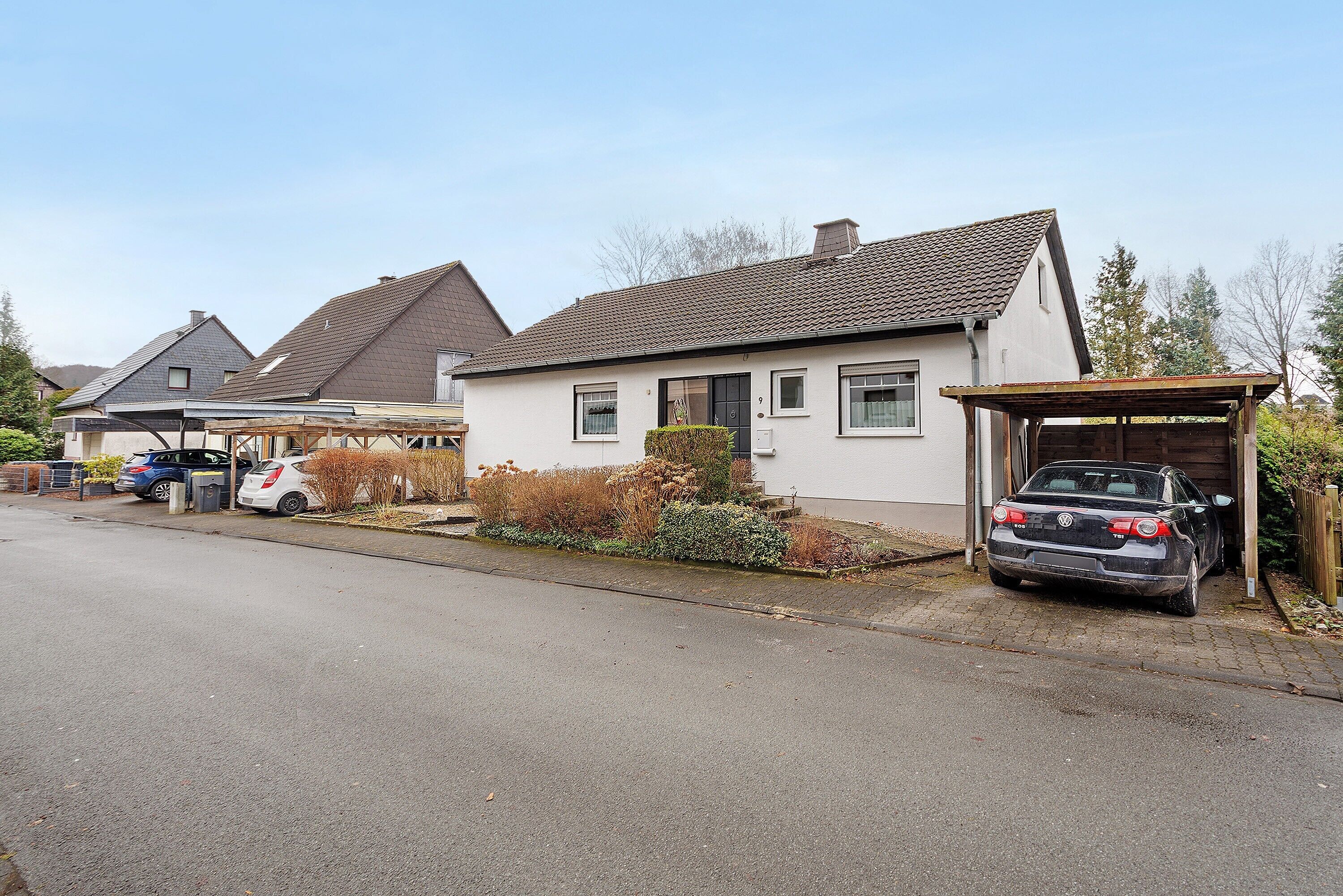Une rue résidentielle bordée de maisons, de voitures garées et d’un garage.