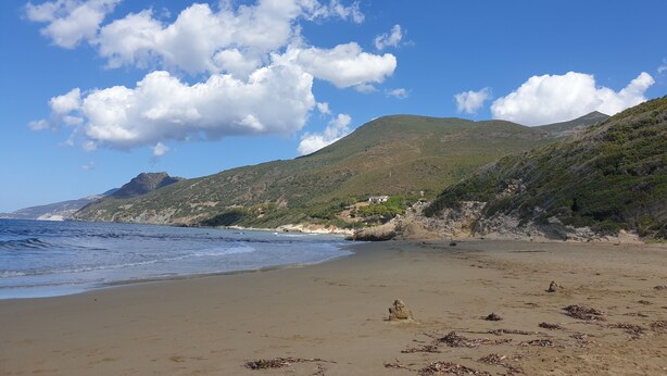 Ein Strand mit blauem Himmel, ruhiger See und einem Berg im Hintergrund.