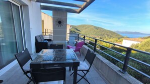 Ein Balkon mit Glastisch und Stühlen, einer Uhr und Blick auf das Meer und die Hügel.