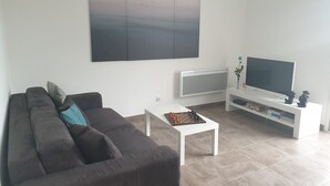 Ein modernes Wohnzimmer mit einem dunkelgrauen Sofa, einem weißen Couchtisch, einem Flachbildfernseher auf einem weißen Schrank und einem großen abstrakten Gemälde an der Wand.