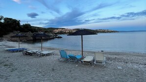 Une plage avec plusieurs chaises longues et des parasols, un rivage rocheux et une mer calme.