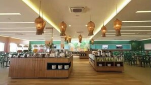 Un restaurant spacieux doté de plusieurs espaces de restauration, de luminaires suspendus et d’un comptoir central où sont présentés divers plats.