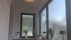 Een gang met een groot raam, een radiator en een hanglamp.