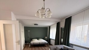 Een moderne kamer met een bed, een slaapbank, een tafeltje en een raam met gordijnen.