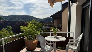 Een balkon met een tafel, stoelen, potplanten en uitzicht op een heuvellandschap.