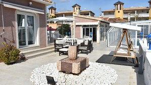 Un patio con mobiliario exterior, una maceta decorativa y un edificio de techos blancos con balcones.
