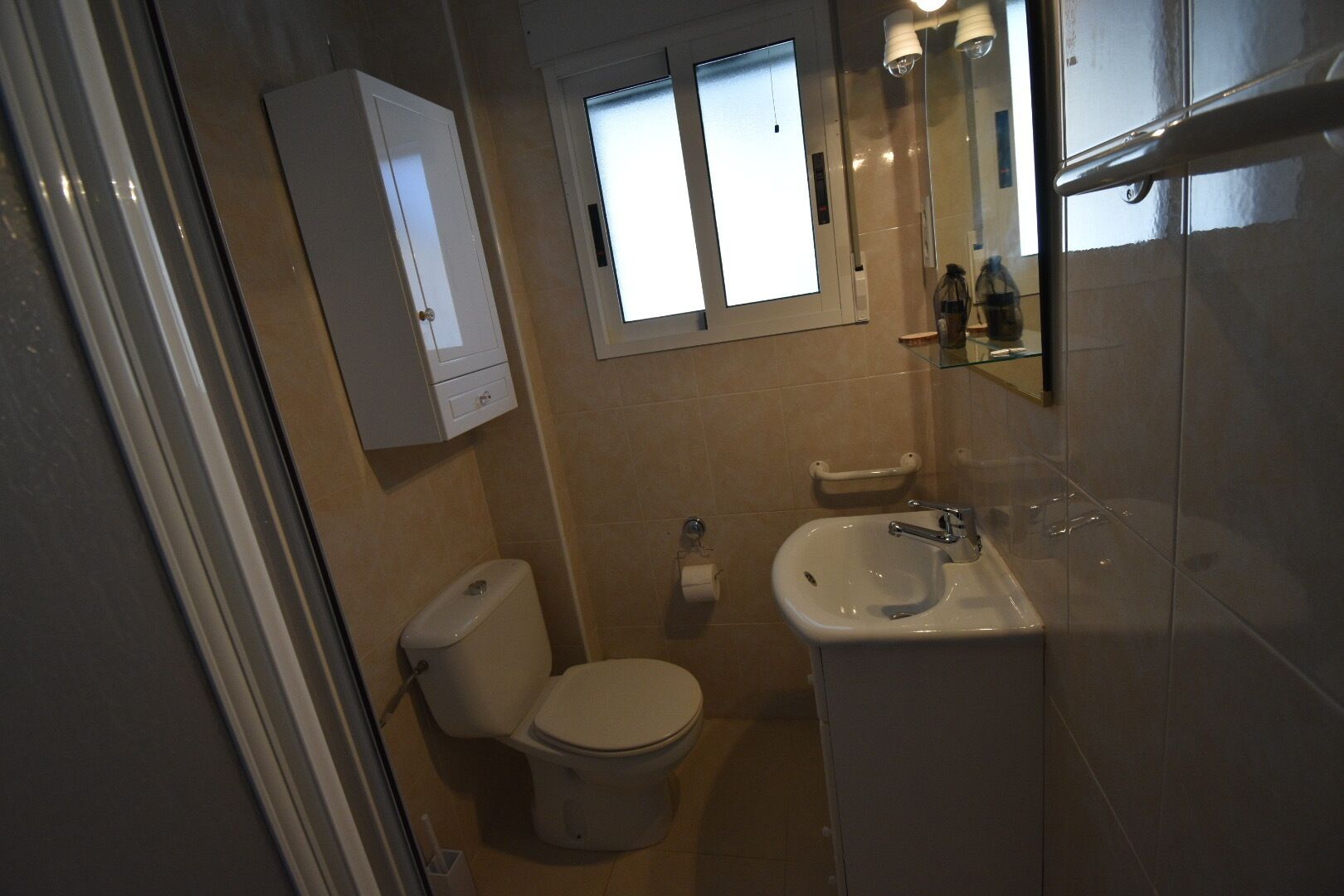 Een kleine, praktische badkamer met toilet, wastafel en spiegel.
