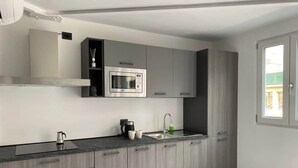 A modern kitchen with grey cabinetry, a stainless steel microwave, a kettle, and a sink.