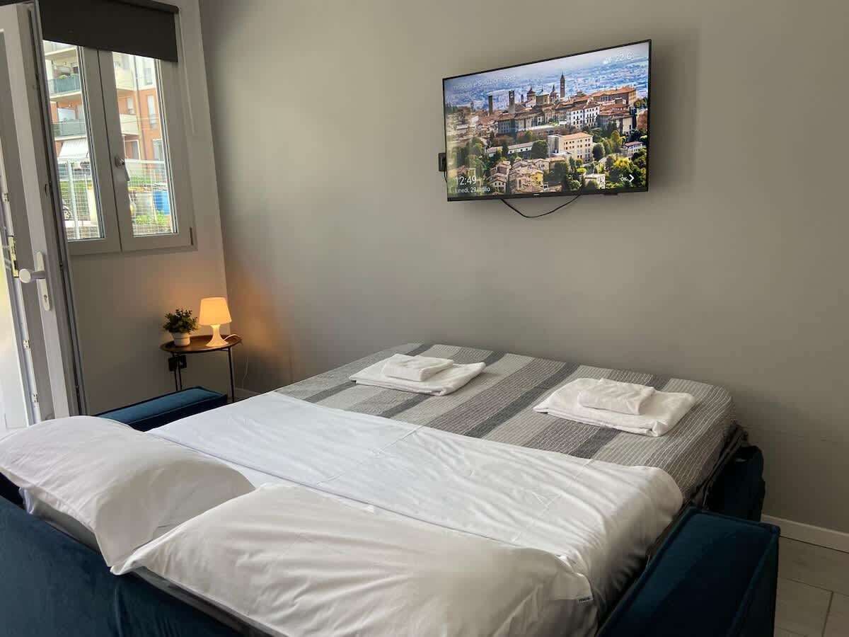 Ett hotellrum med en säng, en tv på väggen och ett fönster med persienner.