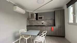 A compact kitchen with a microwave, a sink, and grey cabinets. There is a dining table with two chairs.