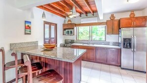 A kitchen with a wooden ceiling, granite countertop, stainless steel appliances, and a large window. - Casa Grande at Flamingo Beach - Family Vacation in Costa Rica (Angeles)