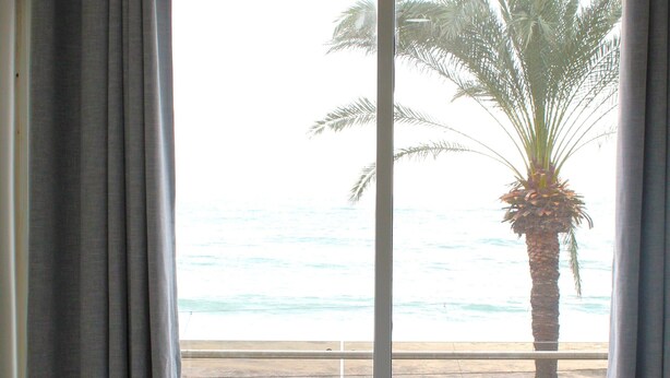 A room with a view of the beach, a chair, a table with a tissue box, and a palm tree. - Voya Hotel and Suites (Tyre)