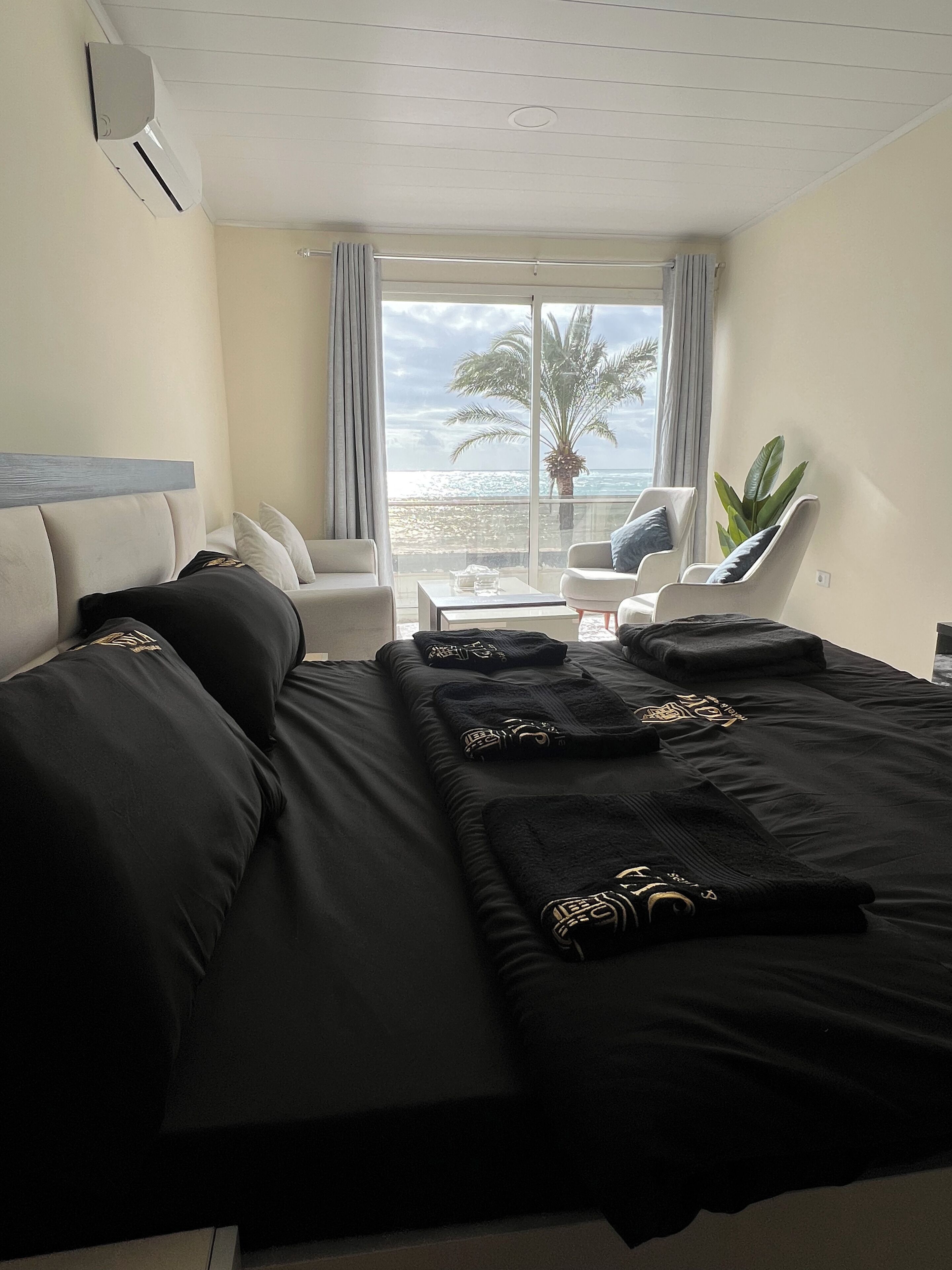 Habitación de hotel con una cama grande, un sofá, una silla y vista al océano.